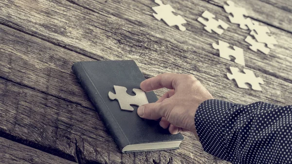 Person platziert ein Puzzleteil auf einem Buchumschlag — Stockfoto