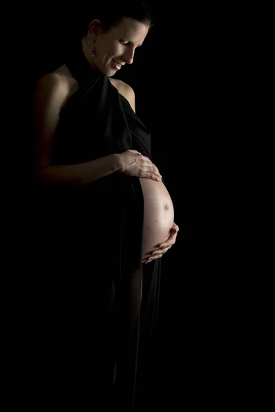 Беременная женщина держит живот изолированным на черном фоне — стоковое фото