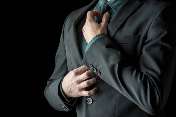 Businessman in green shirt and suit adjusting his black necktie