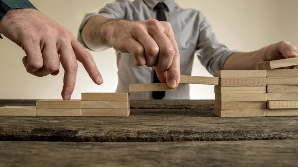 Businessman building staircase with wooden blocks to span a gap — Stock Photo, Image