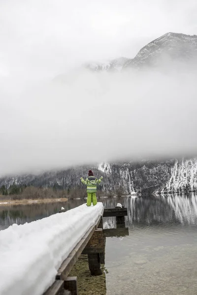 Дитина в зимовому костюмі стоїть на засніженому пірсі на озері — стокове фото
