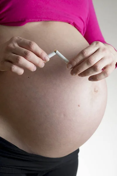 Mulher grávida quebrando um cigarro ao meio — Fotografia de Stock