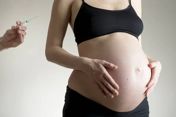 Mujer joven embarazada y una mano con jeringa —  Fotos de Stock