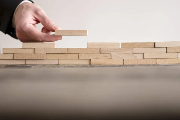 Männliche Hand vervollständigt Bauwand aus Holzsteinen — Stockfoto