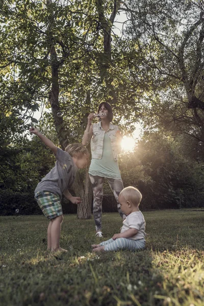 Mladá matka foukání mýdlové bubliny na své dvě děti — Stock fotografie
