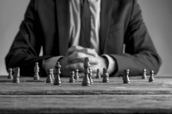 Geschäftsmann im Anzug sitzt vor dunklen Schachfiguren — Stockfoto