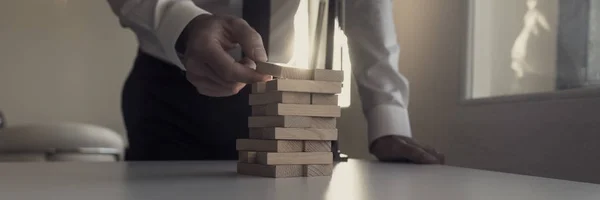 Businessman building tower of wooden bricks with a bright light — Stock Photo, Image