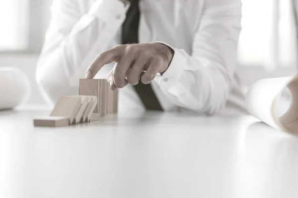 Man preventing dominoes from crumbling on a white office table — Stock Photo, Image