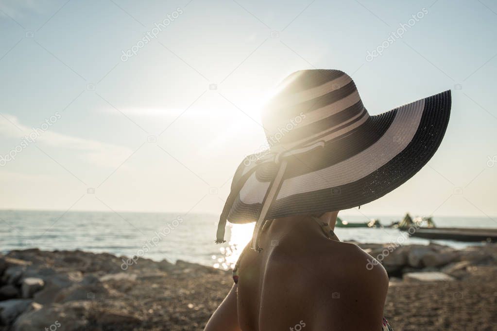 Rear view of woman in swimsuit at the beach watching sunset over