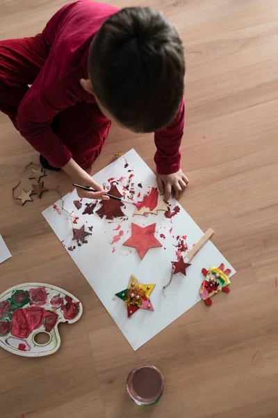 Giovane bambino che fa decorazioni natalizie inginocchiato sul pavimento — Foto Stock