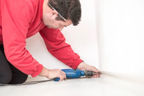 Man worker in red shirt kneeling on the floor drilling a hole — Stock Photo, Image