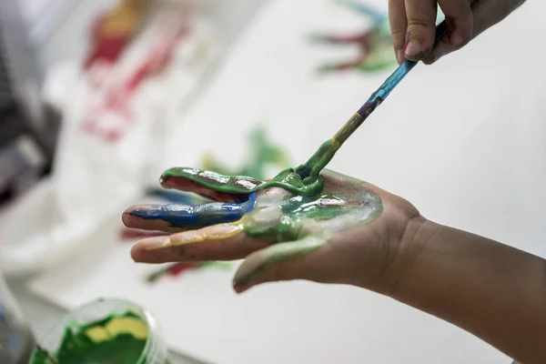 Criança pintando suas mãos com tinta colorida — Fotografia de Stock