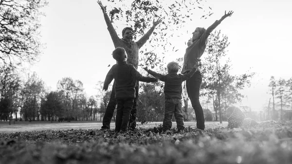 Giovane famiglia che gioca con le foglie autunnali in un grigiastro monocromatico — Foto Stock