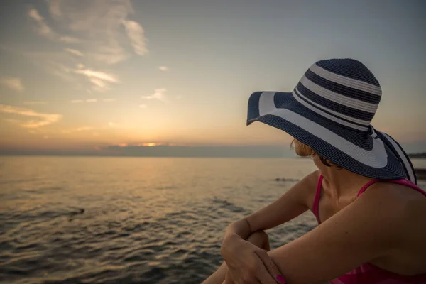 Woman in a trendy straw sunhat relaxing on a beach looking out o — Stock Photo, Image