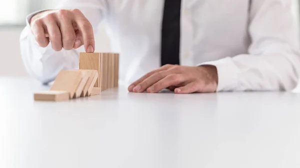 Businessman preventing dominoes from crumbling with finger — Stock Photo, Image