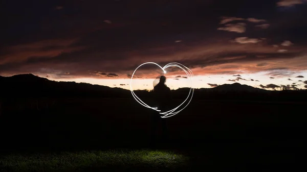 La silueta de un hombre dibuja una forma de corazón con una linterna throug —  Fotos de Stock