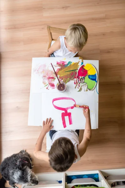 Vista ad alto angolo di due bambini che dipingono su un piccolo tavolo bianco — Foto Stock