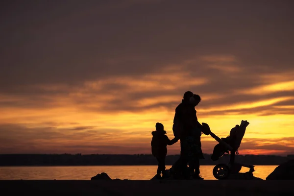 Joven familia silueta contra una puesta de sol en el océano —  Fotos de Stock