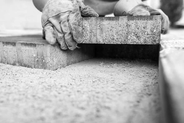 Imagen a escala de grises del trabajador colocando un ladrillo de pavimentación —  Fotos de Stock