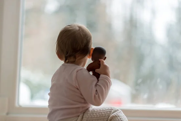 Niña abrazando un juguete mirando la nieve de invierno al aire libre — Foto de Stock