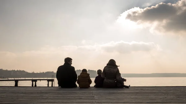 Familia joven sentada en una cubierta de madera al atardecer —  Fotos de Stock