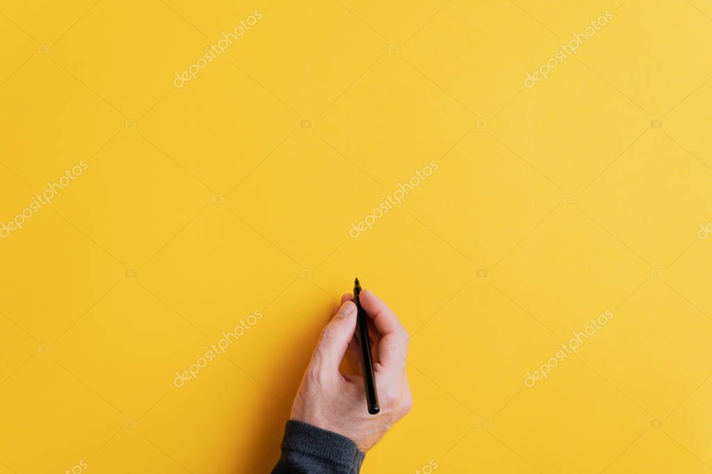 Male hand writing on a blank yellow surface with black marker. With copy space ready for your text, message or promotion.