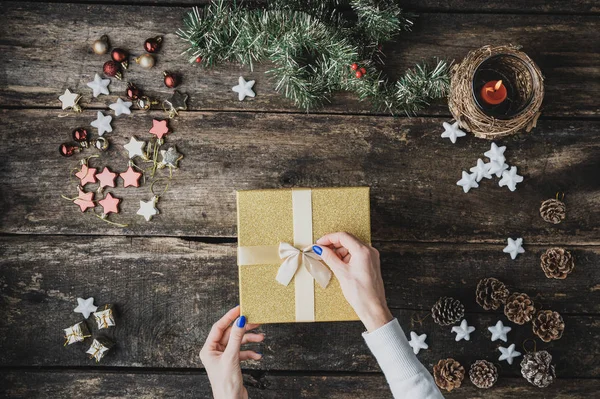 Bovenaanzicht van vrouwelijke handen die een strik plaatsen op gouden vakantiegeschenkdoos — Stockfoto