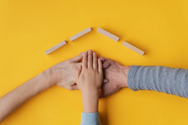 Família empilhando sua mão no fundo amarelo com telhado feito o — Fotografia de Stock