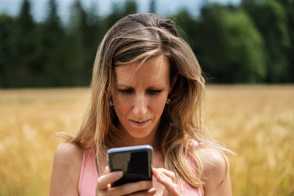 Młoda kobieta patrzy na telefon na zewnątrz — Zdjęcie stockowe