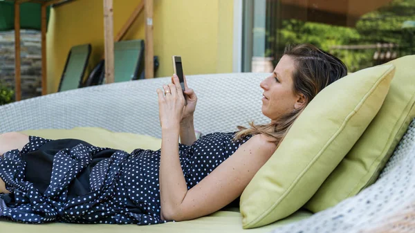 Giovane donna sdraiata sul divano patio sfogliando il suo telefono cellulare — Foto Stock