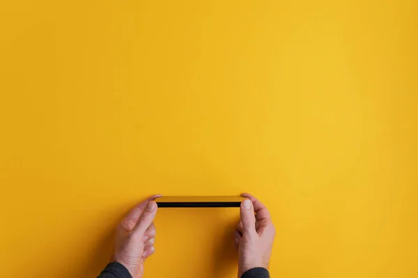 男性手保持黒スマートフォン上の黄色の背景 — ストック写真