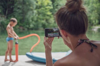 Genç anne oğlunun cep telefonuyla fotoğrafını çekiyor.
