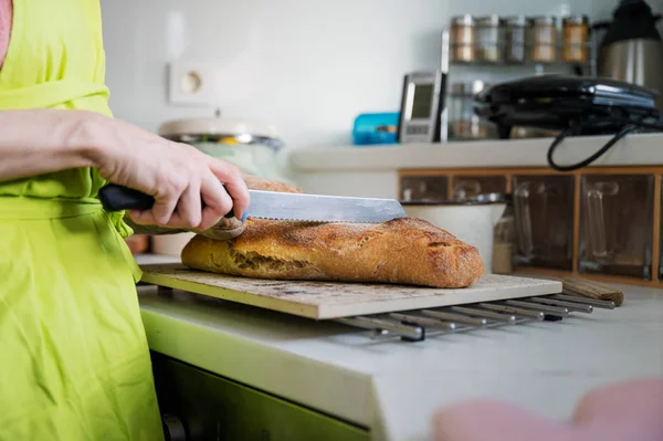 Woman wearing green apron cutting freshly baked home made sourdo — 스톡 사진