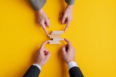 İş dünyası kavramsal imajı. Bir iş adamı ve iş kadınının elleri boş tahta çiviler yığıyor. Sarı arkaplan.