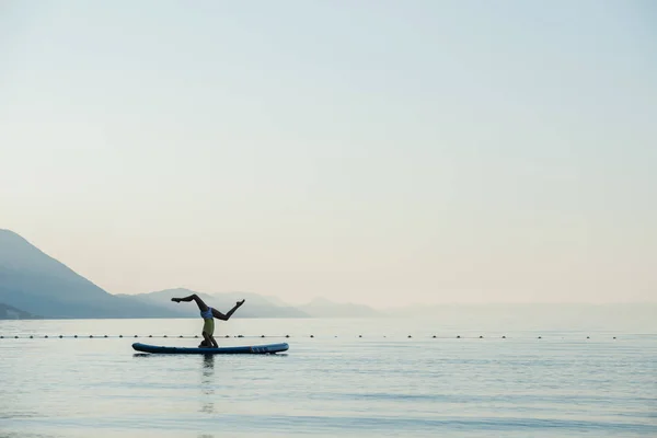 朝の海の穏やかな水の上に浮かぶアップボード上で頭を作る若い女性をフィット — ストック写真