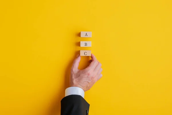 一个商人的手把三个木制块与字母A B和C的黄色背景 业务规划和不同选择的概念形象 — 图库照片
