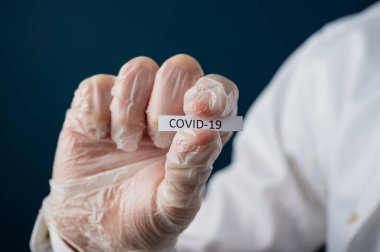 Elinde Covid 19 işareti olan koruyucu eldiven giyen bir doktorun yakın çekimi. Halk sağlığını tehdit eden virüsün kavramsal görüntüsü.