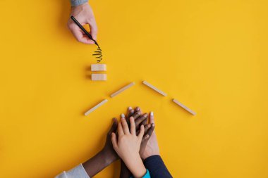 Karışık ırk ailesi için ahşap bloklardan ev inşa eden bir babanın eli. Aile değerleri ve evlat edinme kavramsal imajı.