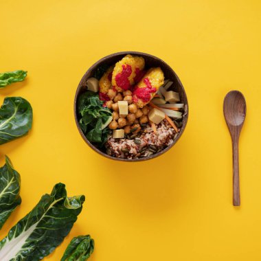 Hindistan cevizi Buda kasesinde servis edilen lezzetli ve dengeli vejetaryen yemeğinin üst görüntüsü. Yanında da sarı arkaplan ve taze İsviçre çedarlı..