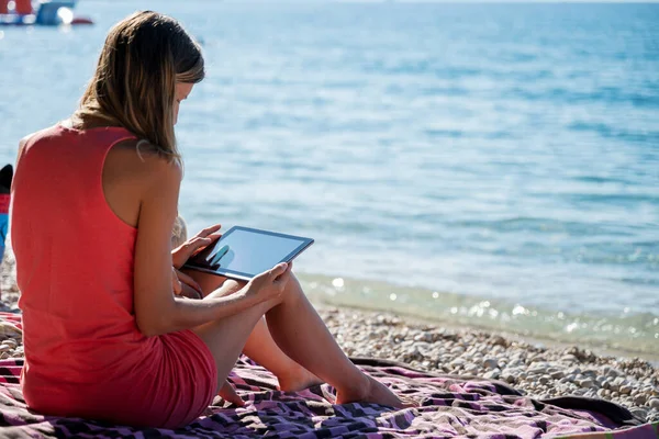 Młoda Kobieta Siedząca Ręczniku Plażowym Nad Rannym Morzem Przeglądająca Tablecie — Zdjęcie stockowe