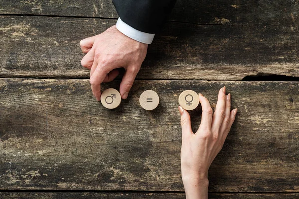 Gender equality conceptual image - male and female hand placing wooden cut circles with gender symbols over rustic wooden desk.