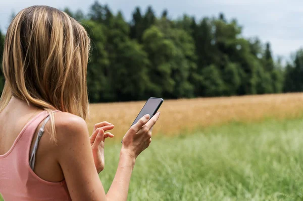 フィールドと草原の夏の性質に立って若い女性彼女の携帯電話でブラウジング — ストック写真