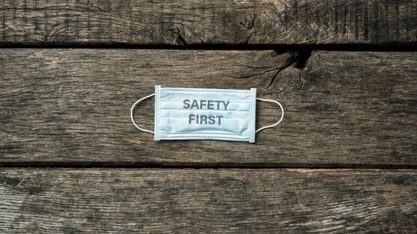 Safety first sign printed on medical protective mask placed over rustic wooden background.