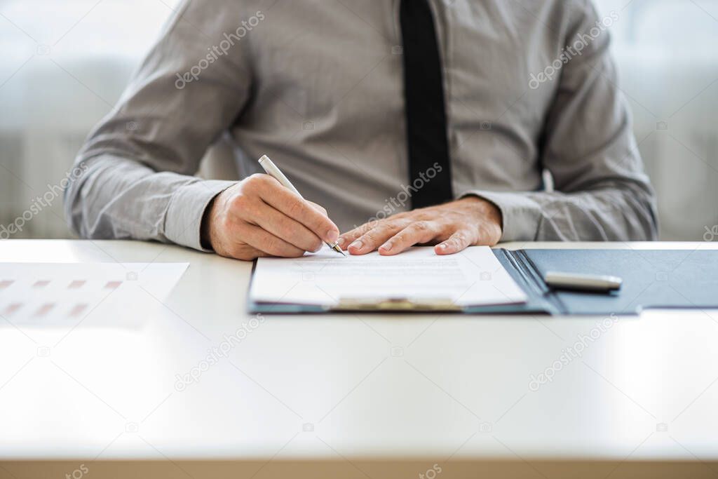 Businessman or lawyer sitting at his desk signing a document or contract.