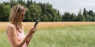 Yazın doğa yürüyüşü sırasında cep telefonunda gezinen genç bir kadının profil görüntüsü. 