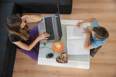 Evde eğitim kavramsal görüntüsü - dizüstü bilgisayarda oğlunun yanında çalışan genç annenin matematik öğrenmesi ve ödev yapması..