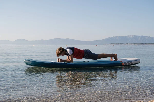 平和的な穏やかな朝の海の水に浮かんでボード上の板のポーズを保持作業若い男をフィット — ストック写真