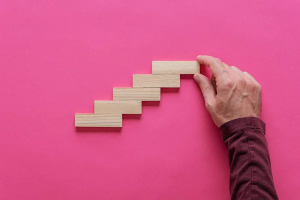 雄鸟的手在粉红色的背景上用木钉做成楼梯状的结构 增长与发展的概念形象 — 图库照片