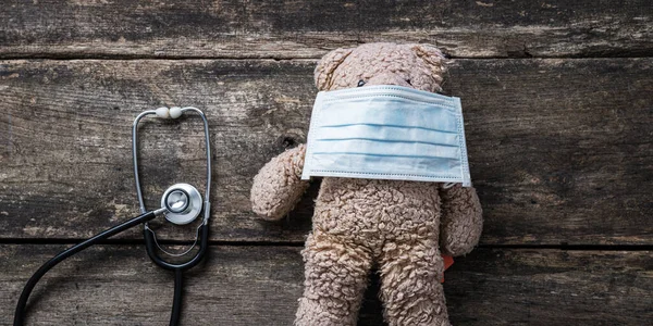 在儿科健康护理的概念图中 泰迪熊戴着防护医疗面罩 旁边是听诊器的头像 — 图库照片