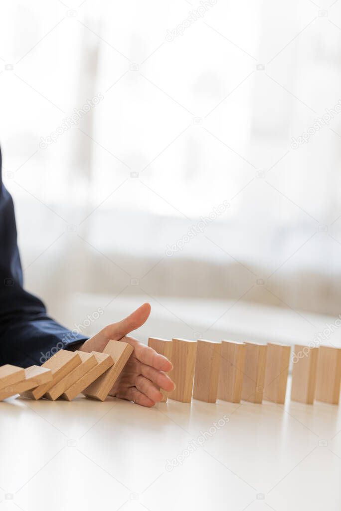Closeup view of hand of a businesswoman stopping collapsing dominos in financial crisis management conceptual image.